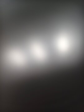 Abstract blurry background of three glowing white lights on a dark grey gradient surface.