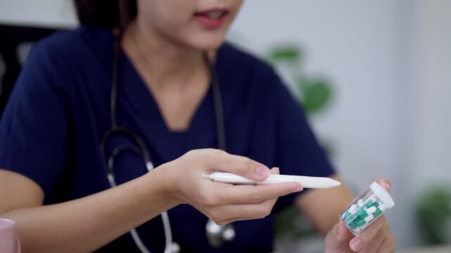Young Asian female doctor explaining medication dosage while holding pill bottle and pen in clinic