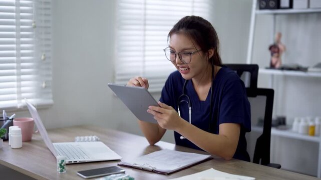 Young Asian female doctor reviewing digital tablet at desk in bright medical office
