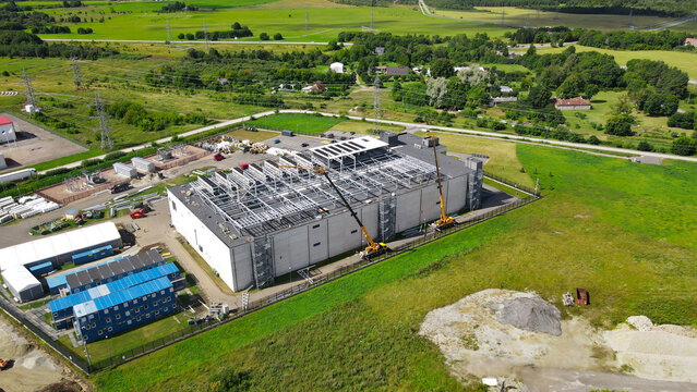Aerial view showing a large data center building under construction with cranes, workers, equipment, and cooling systems on the rooftop in a rural industrial area