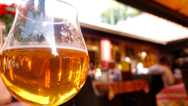 Golden beer glass being filled with foamy head on a sunlit outdoor restaurant table, close up with bokeh background conveying refreshing summer leisure and relaxation