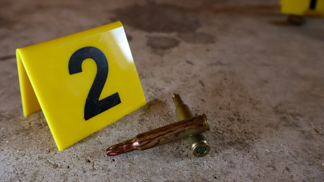 Forensic team documents crime scene on dirty concrete floor, collecting bullet casings and marking potential blood traces with evidence markers during police investigation and analysis