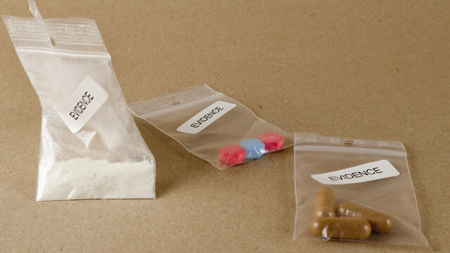 Forensic evidence bags with white powder, colorful pills, and brown capsules, sealed and labeled, representing illegal drugs confiscated during a police investigation or crime scene processing