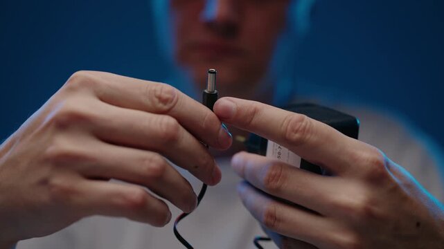 Close-up of person hands connecting coaxial power connector to black electrical adapter, concept of power supply, charging, electrical connectivity. Shooting in slow motion.
