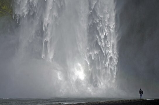 A man stands in front of an impressive waterfall, surrounded by splashing spray, Skogafoss, Iceland