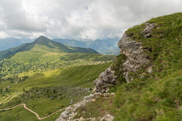 Fototapeta premium Italy. Green alpine landscape with rugged limestone cliffs, mountain trails and distant Dolomite peaks