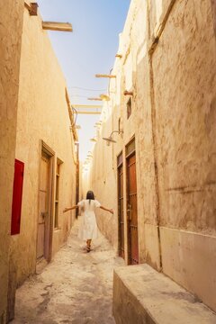 Doha Qatar Katara Cultural Village woman walking narrow traditional alley mud brick walls heritage architecture sun flare travel tourism Middle East Qatari culture exploration sunny