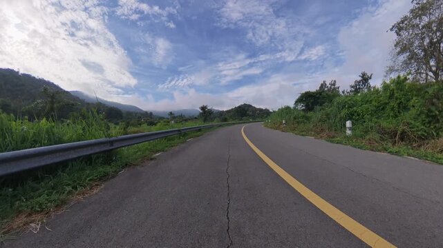 Scenic winding road through lush green vegetation with forested hills and a dramatic blue sky, creating a peaceful tropical travel landscape.