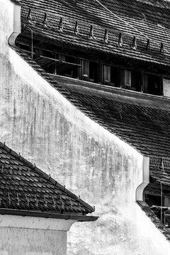 Black and white detailed view of an angled roofline, traditional roof tiles, and weathered plaster wall of a historic building in Frohnleiten, Styria, Austria