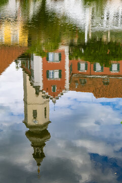 Mirrored water reflection on the Mur River displaying the parish church tower and historic step-gabled architecture of Frohnleiten in Styria, Austria