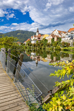 View from a wooden footbridge across the Mur River leading toward the historic town skyline and parish church tower of Frohnleiten in Styria, Austria