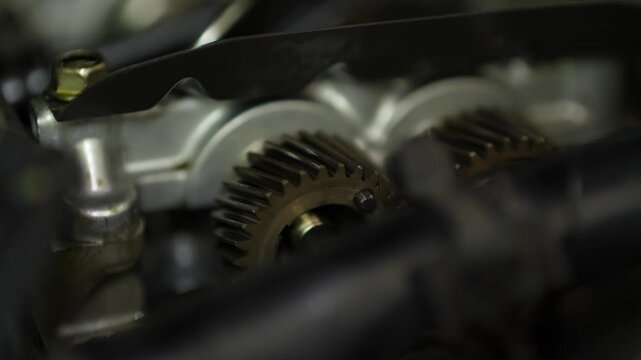 A selective focus close-up highlights interlocking metallic camshaft gears inside an opened cylinder head of a car engine.