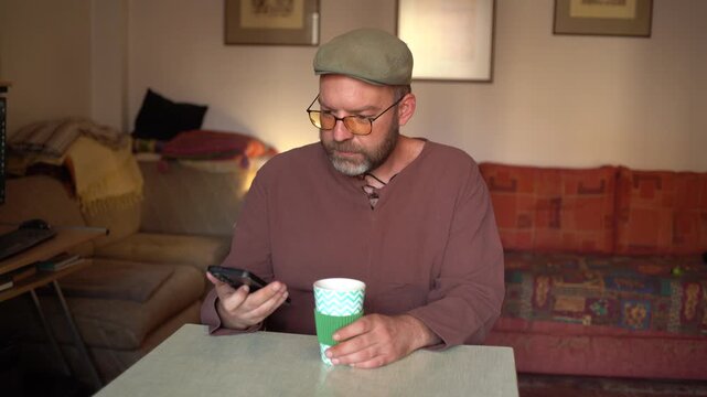 Mature handsome man at home using phone and drinking coffee