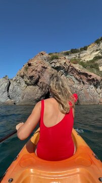 Kayaking woman summer, active female tourist canoeing in red swimsuit near rocky cliffs on sunny ocean sea water during outdoor tropical holiday adventure