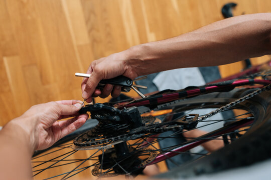 Mechanic performing bicycle maintenance. Person tuning gears and drivetrain on bicycle wheel indoors. Hobby, transport repair, active lifestyle concept. Close-up with wooden floor background.