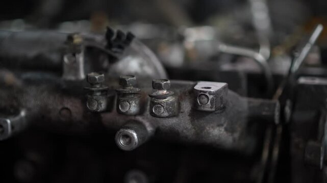A close-up shot captures three rusty mounting bolts securing a metallic manifold bracket component onto a car engine cylinder block.