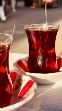 Traditional Turkish tea served in classic tulip shaped glasses with red pattern saucers. Hot amber beverage close up on a cozy local street cafe background.
