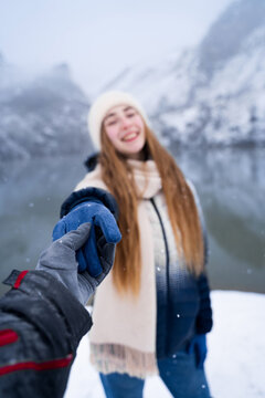 Follow me concept in winter mountains, woman holding partner hand near lake, travel adventure, relationship and outdoor lifestyle theme. Selective focus on hands.