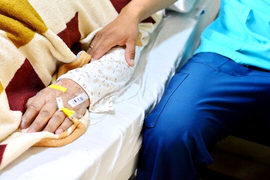 The hand of medical worker holding senior patient's arm with catheter. No faces can be seen.