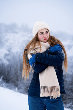 Woman freezing in cold winter weather, humorous facial expression, outdoor lifestyle, seasonal cold and weather concept. Front view portrait.