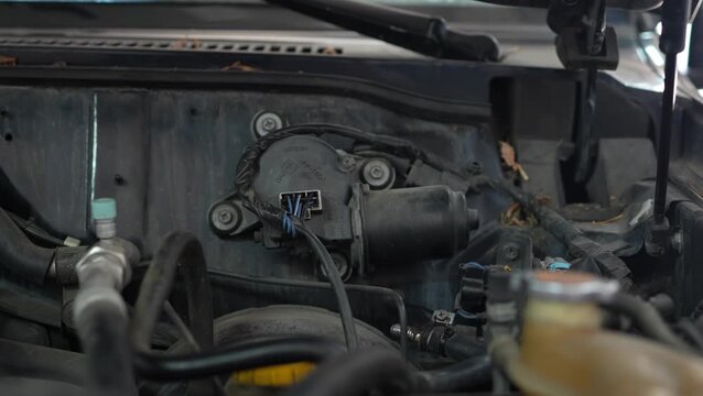 A black electric windshield wiper motor assembly with electrical connectors and wires is mounted on a car firewall partition.