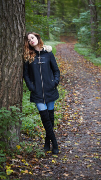 Thoughtful Young Woman Leaning Against Tree in Autumn Forest with Sad and Contemplative Mood