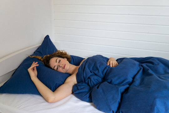 Peaceful Woman Sleeping in Bed Under Blue Bedding as Rest and Healthy Sleep Concept