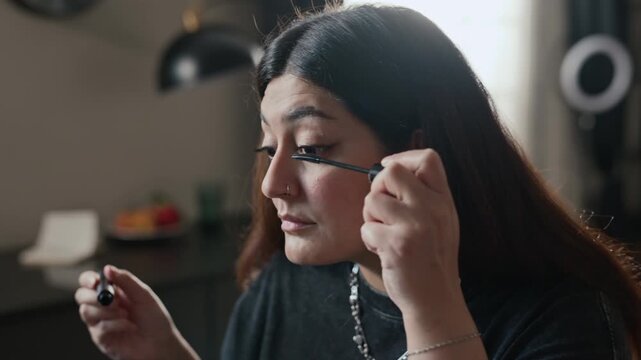 Young adult woman applying black mascara to eyelashes with wand, looking into mirror. Footage is ideal for cosmetics advertising, beauty tutorials, and makeup brand promotions