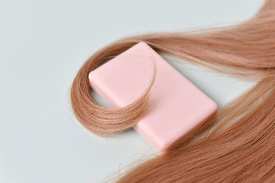 Hair shampoo soap bar surrounded by hair on light mint green background