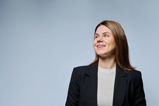 Smiling adult businesswoman looking up to side with copy space on grey background