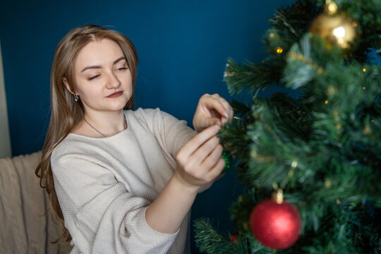 Woman decorate Christmas tree with red ornament at home
