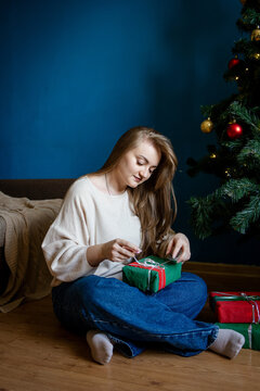 Woman wrap Christmas gift beside decorated tree at home