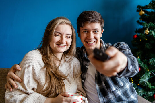 Young couple watch television with remote at Christmas