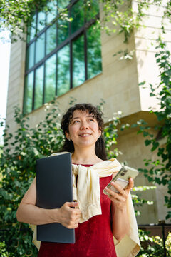 Female student with laptop and smartphone outside university