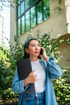 Student with laptop talk on smartphone outside campus