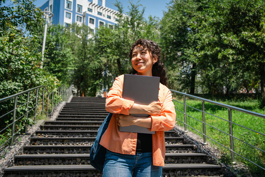 Smiling student with laptop on urban campus staircase