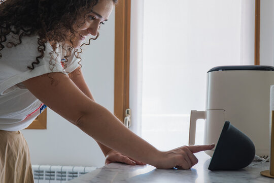 Woman use smart home device with air fryer in apartment