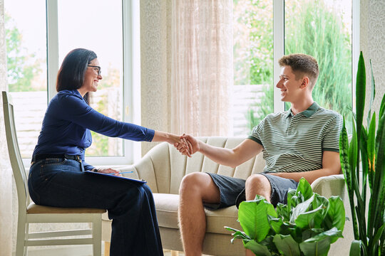 Female psychologist shaking hands with teenage boy sitting on sofa in office