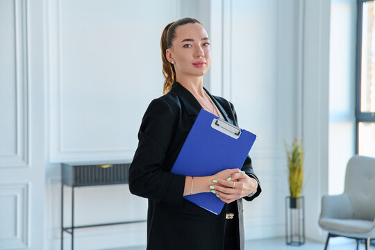 Confident businesswoman holding blue clipboard folder in modern office