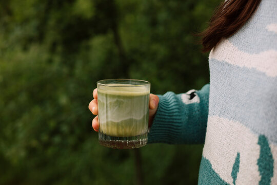 Woman hold matcha latte outdoors on summer morning