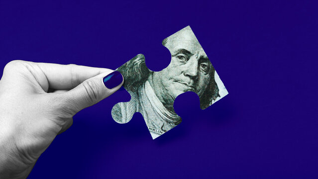 Hand holding a piece of puzzle made from dollar bill showing Benjamin Franklin