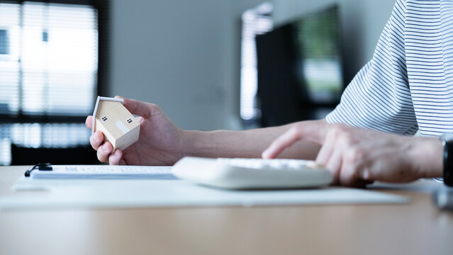 Person holding a house model and using a calculator to plan housing expenses, concept of mortgage calculation, home purchase, budgeting, finance and real estate investment.