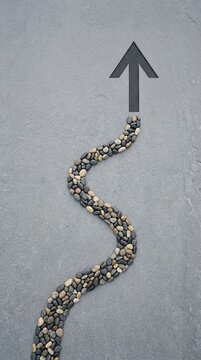 Arrow pointing upwards on a gray surface with a winding path of stones.