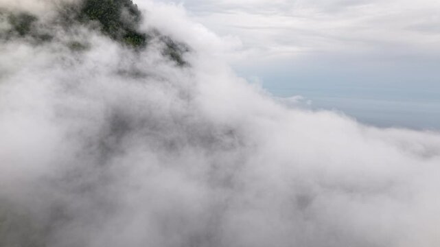 Aerial view of dense fog and clouds rolling over green forested mountain slope in Mont Saint-Pierre Gaspesie Quebec Canada drone footage