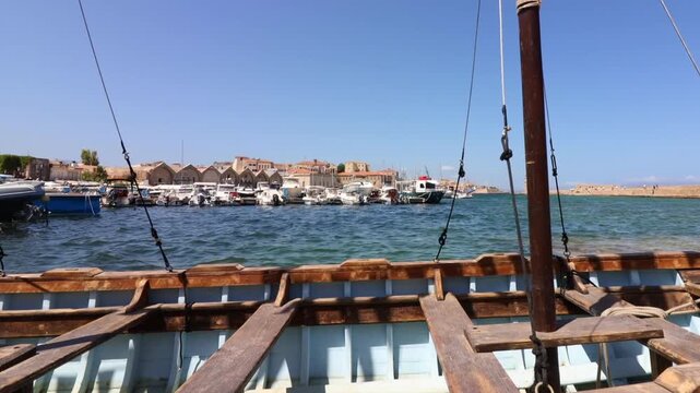 Viewed across a small wooden boat, a Crete marina fills with small boats bobbing in choppy water.