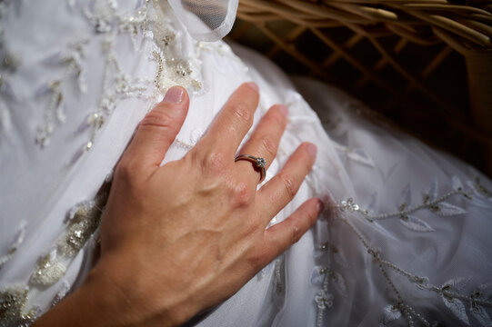Bride hand with wedding ring on embroidered white gown