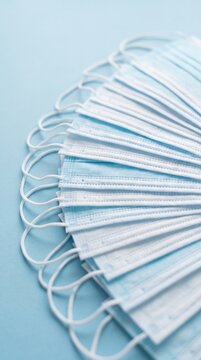 Stack of blue surgical face masks fanned out on a light blue background, medical protective equipment for healthcare and disease prevention.