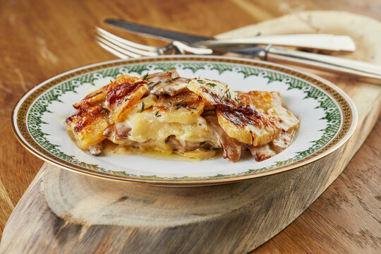 Potatoes with mushrooms, ready-made portion of step-by-step recipe in a vintage plate on a wooden background.