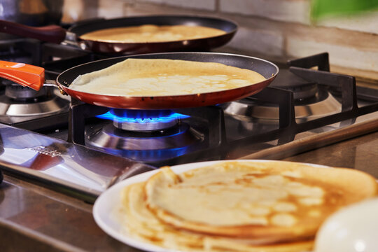 Cooking at home in the kitchen according to recipe from the Internet. Pancakes are fried in pans on a gas oven. Step by step recipe.