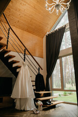 The bride's white dress hangs on a trellis next to a black classic jacket in a country apartment on the newlyweds' wedding day © Olha Cheverda